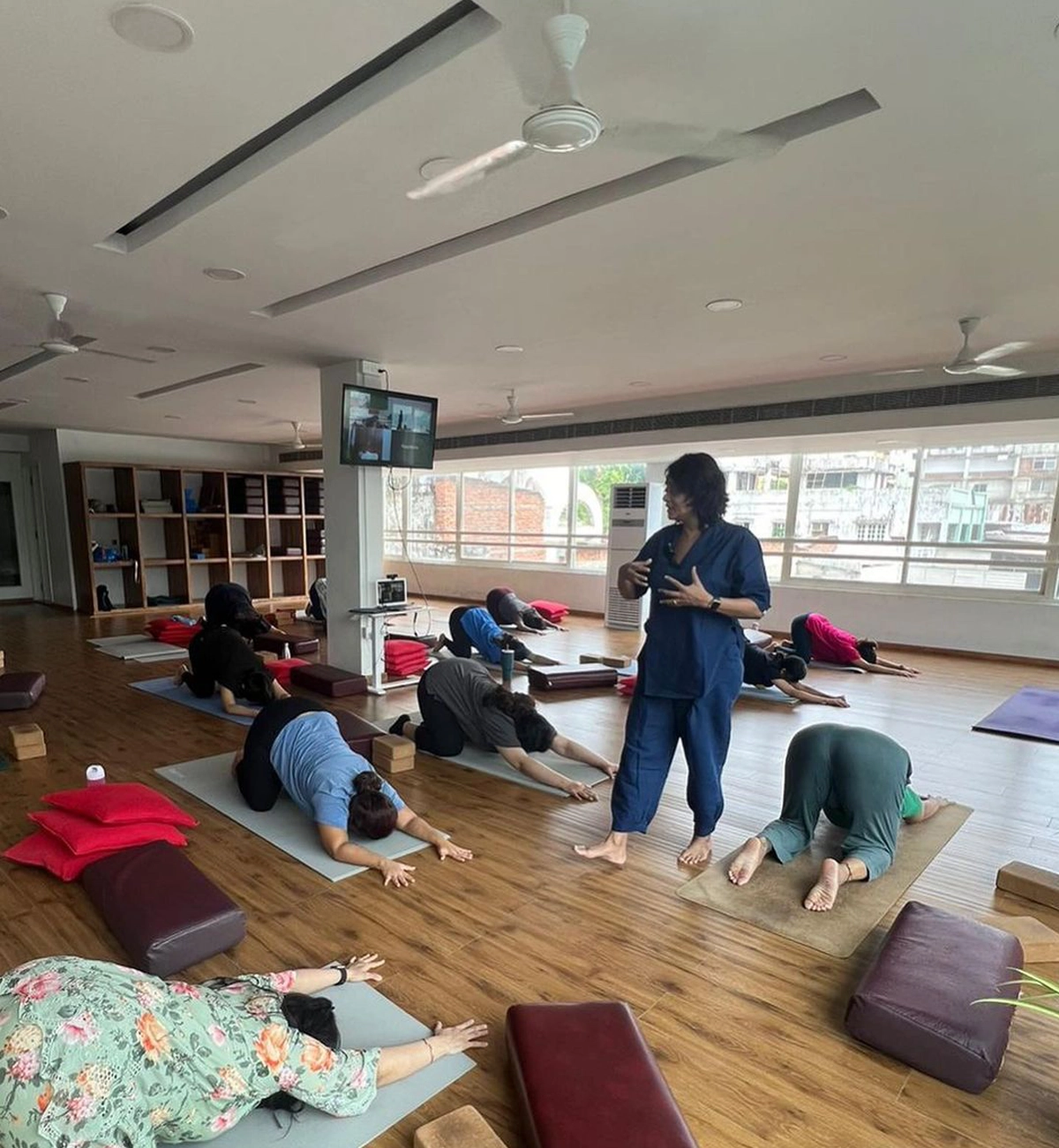 A yoga instructor assisting a man in a child’s pose on a mat inside a peaceful studio.