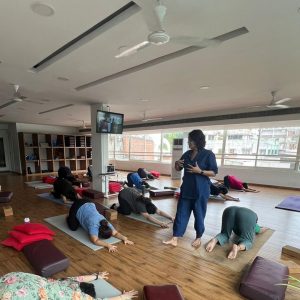 A yoga instructor guiding a class as participants practice child's pose in a spacious studio.