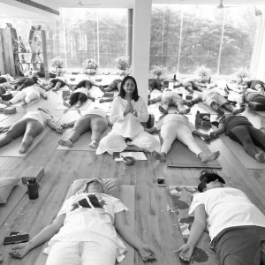 A yoga instructor guiding a class of people lying on mats in a peaceful studio.