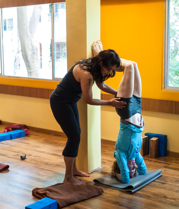 Yoga instructor assisting a student in headstand pose near a wall